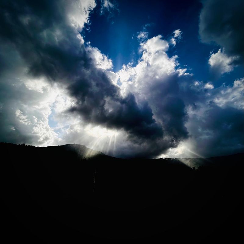 Bright sun shining through clouds against a dark mountain background